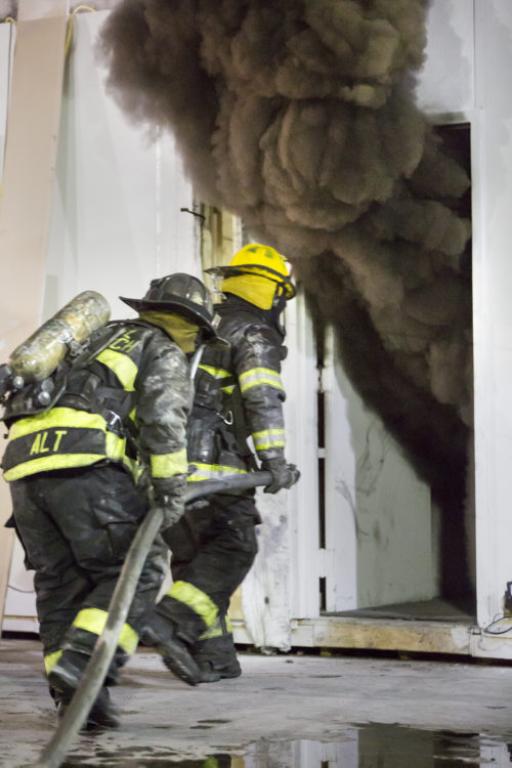 Firefighters entering smoking metal container with fire hose