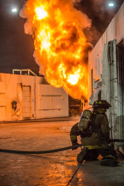 Firefighter entering training structure in front of large flame