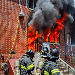 Three fire fighters in front of burning brick building