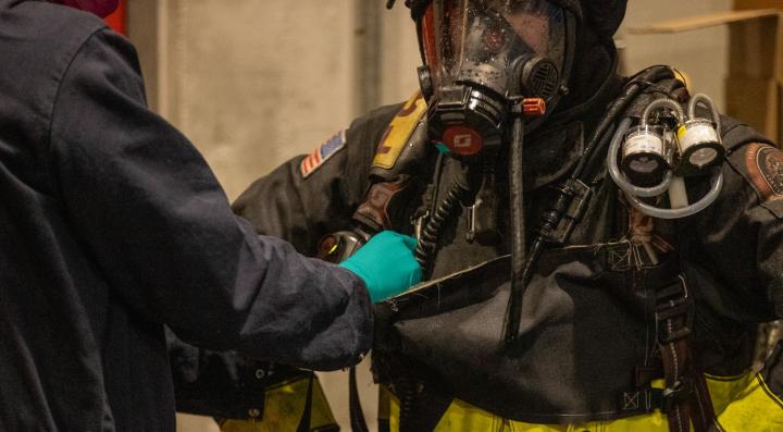 Researcher attaching personal protective equipment swatch on firefighter before vehicle suppression