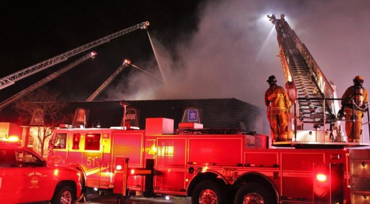 Chula Vista Fire Department crews respond to a warehouse fire. A ladder truck is visible in the foreground, and four extended ladders surround the warehouse, spraying water onto the structure during a near‑miss incident.