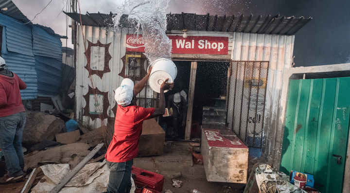Residents of an informal settlement try to fight a fire on their own with limited resources before it spreads to neighboring vulnerable structures