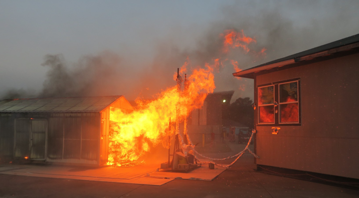 Experiment setup is shown with a test structure, reflective of a California Building Code Chapter 7A-compliant home, exposed to fire from a nearby structure (shed).