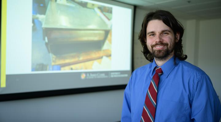 Ian stands in front of his thesis presentation on the use of a phi meter for fire smoke analysis