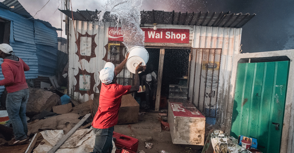 Residents of an informal settlement try to fight a fire on their own with limited resources before it spreads to neighboring vulnerable structures