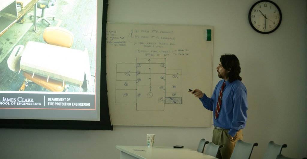 Ian presents his thesis on phi meters, pointing to a presentation slide about fire smoke analysis.