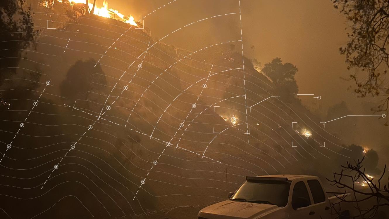 Wildfire spreading across a hillside at night with white contour lines and markers overlaid on top representing wildfire risk modeling
