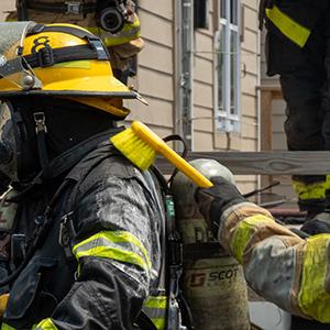 Firefighter in full PPE getting brushed to reduce contamination