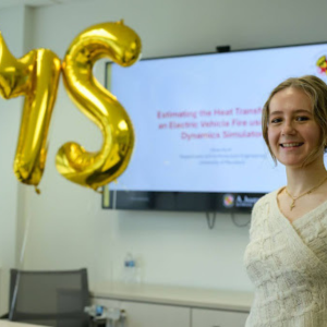Olivita presenting thesis on electric vehicle fire modeling with MS balloons in background